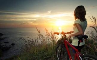 A woman holding a bike, watching the sun set over the sea